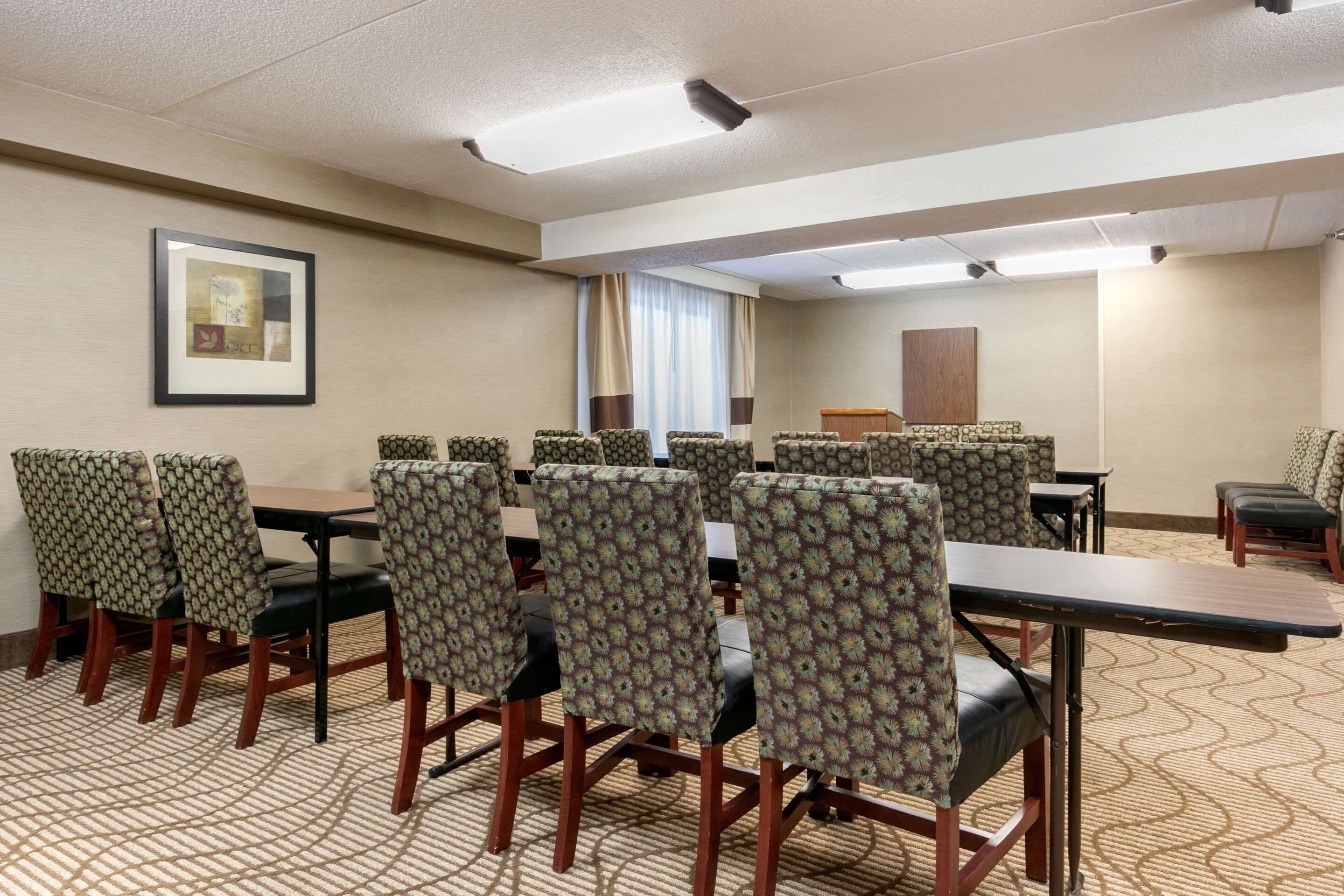 A conference room with multiple tables and chairs, a framed picture on the wall, and a window with curtains.