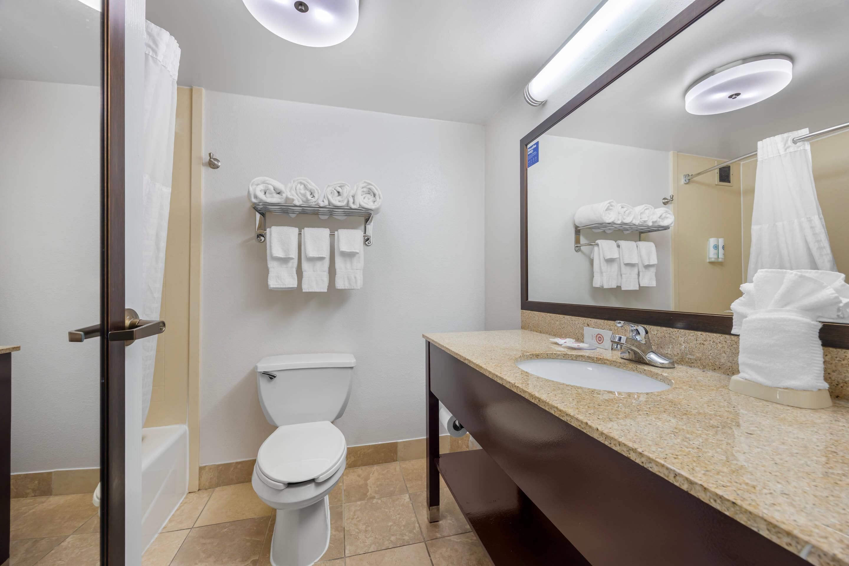 Un baño moderno con inodoro, lavamanos y zona de ducha. Se observan toallas y artículos de aseo.