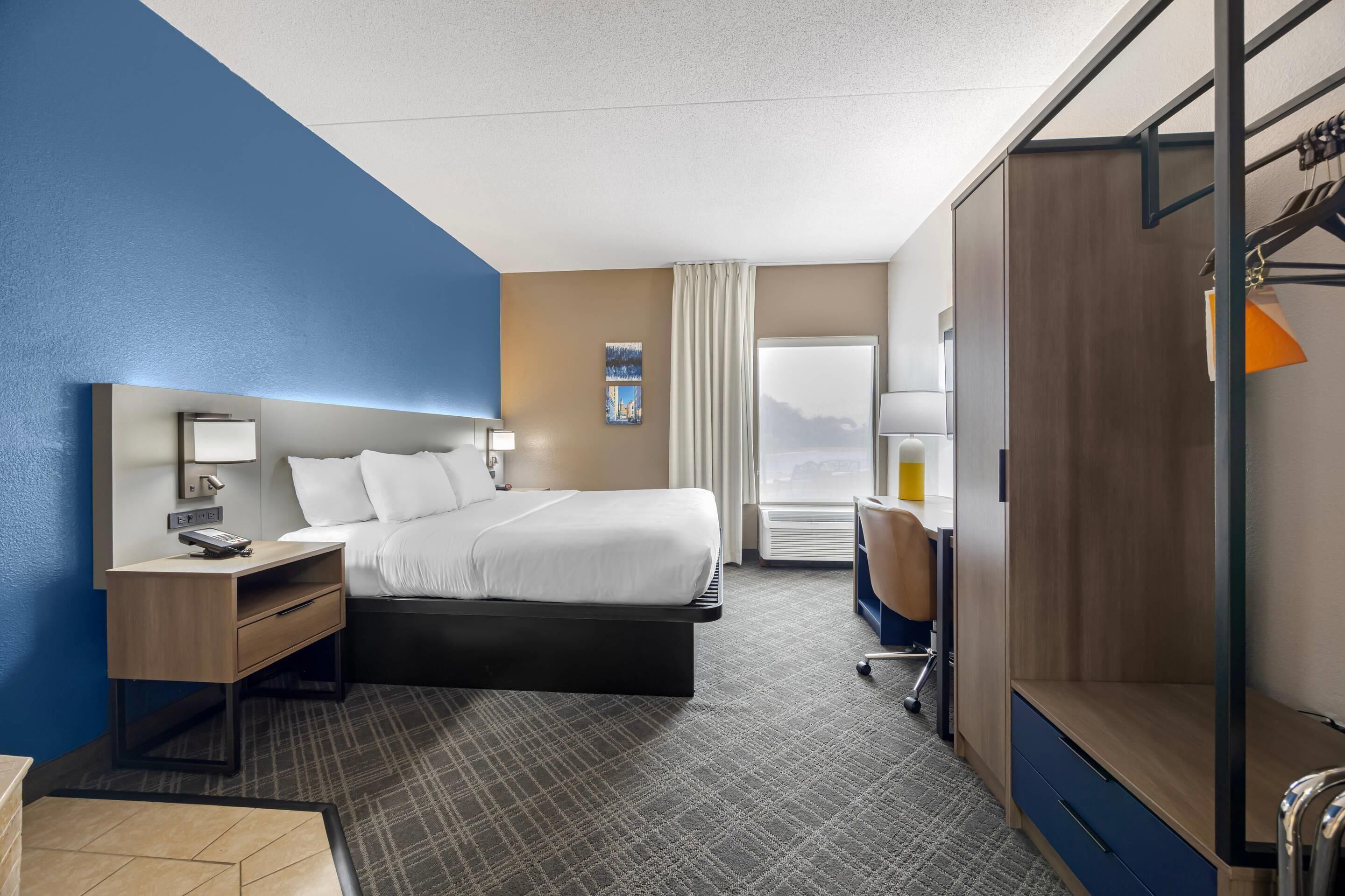 A hotel room with a bed, bedside table, lamp, and a wardrobe.