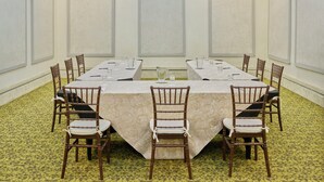 Un salón de conferencias con una mesa larga, sillas y una alfombra estampada.