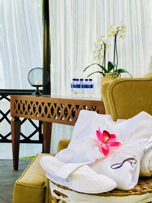 A wicker chair with a white towel and slippers, a bottle of water, and white orchids on a table.