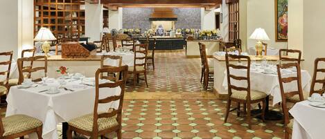 A restaurant with multiple tables set for dining, wooden chairs, and a patterned floor.