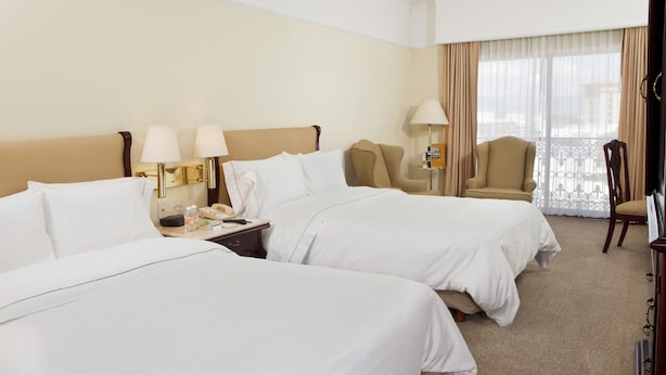 Une chambre d’hôtel avec deux lits, une table de chevet avec un téléphone, des lampes et une chaise près de la fenêtre.