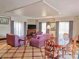 Habitación de hotel con sala de estar, chimenea, mesa de comedor y sillas, y televisor.