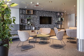 A modern lounge area with seating, a flat-screen TV, and decorative shelves.