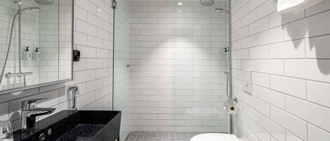 Un baño moderno con lavamanos de granito negro, inodoro blanco y zona de ducha con cerramiento de vidrio.