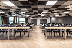 Een vergaderruimte met een geruit plafond, meerdere tafels en stoelen, klaar voor vergaderingen.