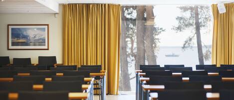 A classroom with rows of desks and chairs, a large window with curtains, and a framed picture on the wall.