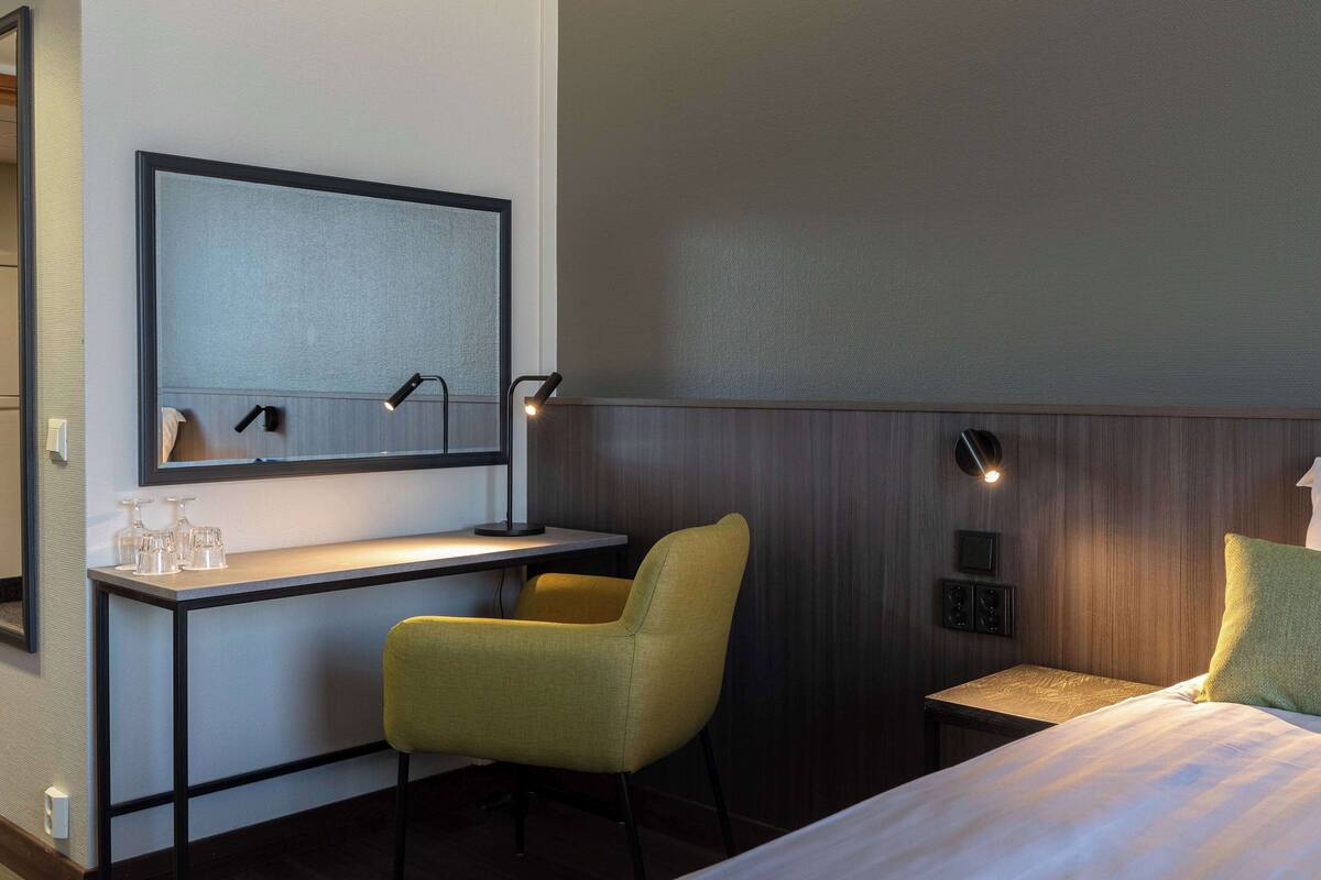 Ein Hotelzimmer mit Bett, Schreibtisch mit Stuhl, Spiegel und Wandleuchten.