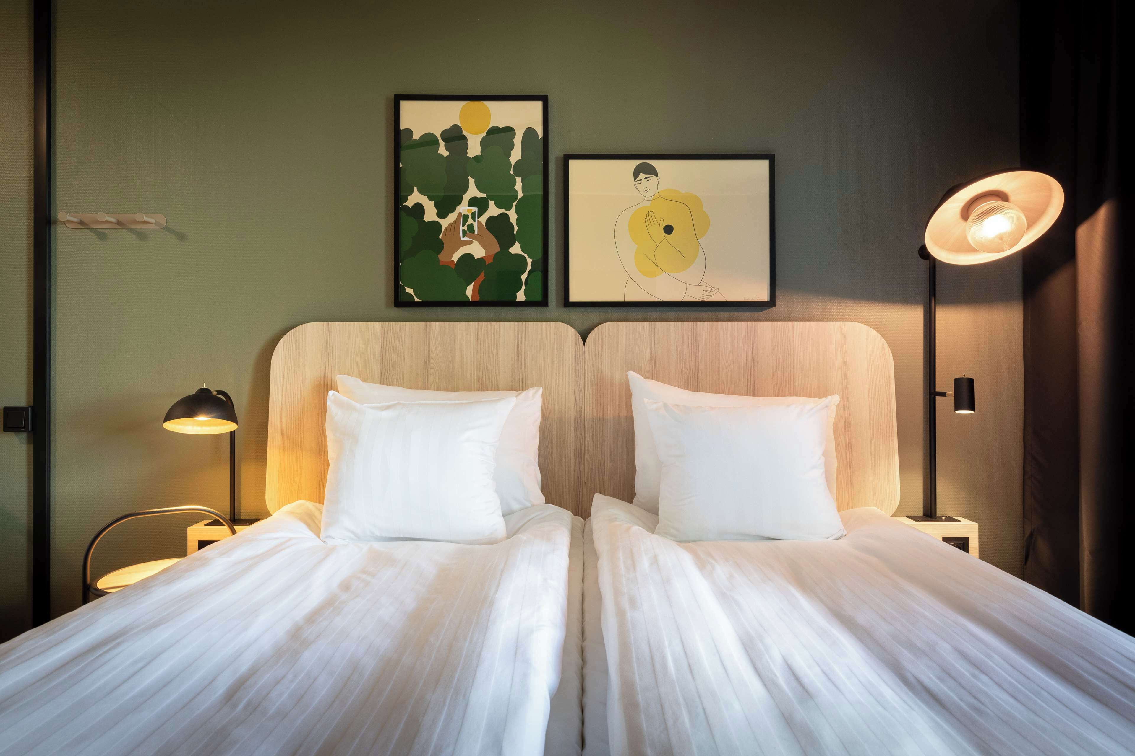 A double bed with white linens, two bedside tables with lamps, and two framed artworks on the wall.
