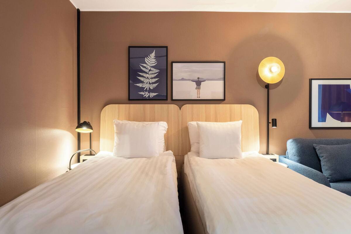 Ein Hotelzimmer mit zwei Betten, einem Nachttisch, einer Lampe und einem Sofa.