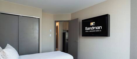 Una habitación de hotel con dos camas, un armario, un televisor y una puerta que da a una cocina.