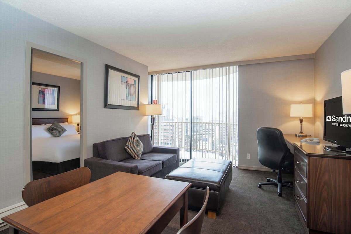 Hotelkamer met een bed, een sofa, een bureau, een televisie en een raam met jaloezieën.
