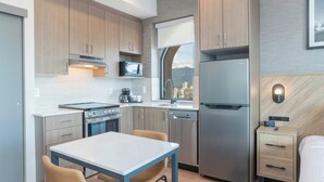 Een compacte keuken met een fornuis, magnetron en koelkast, een eethoek met tafel en stoelen, en een klein nachtkastje met lades.