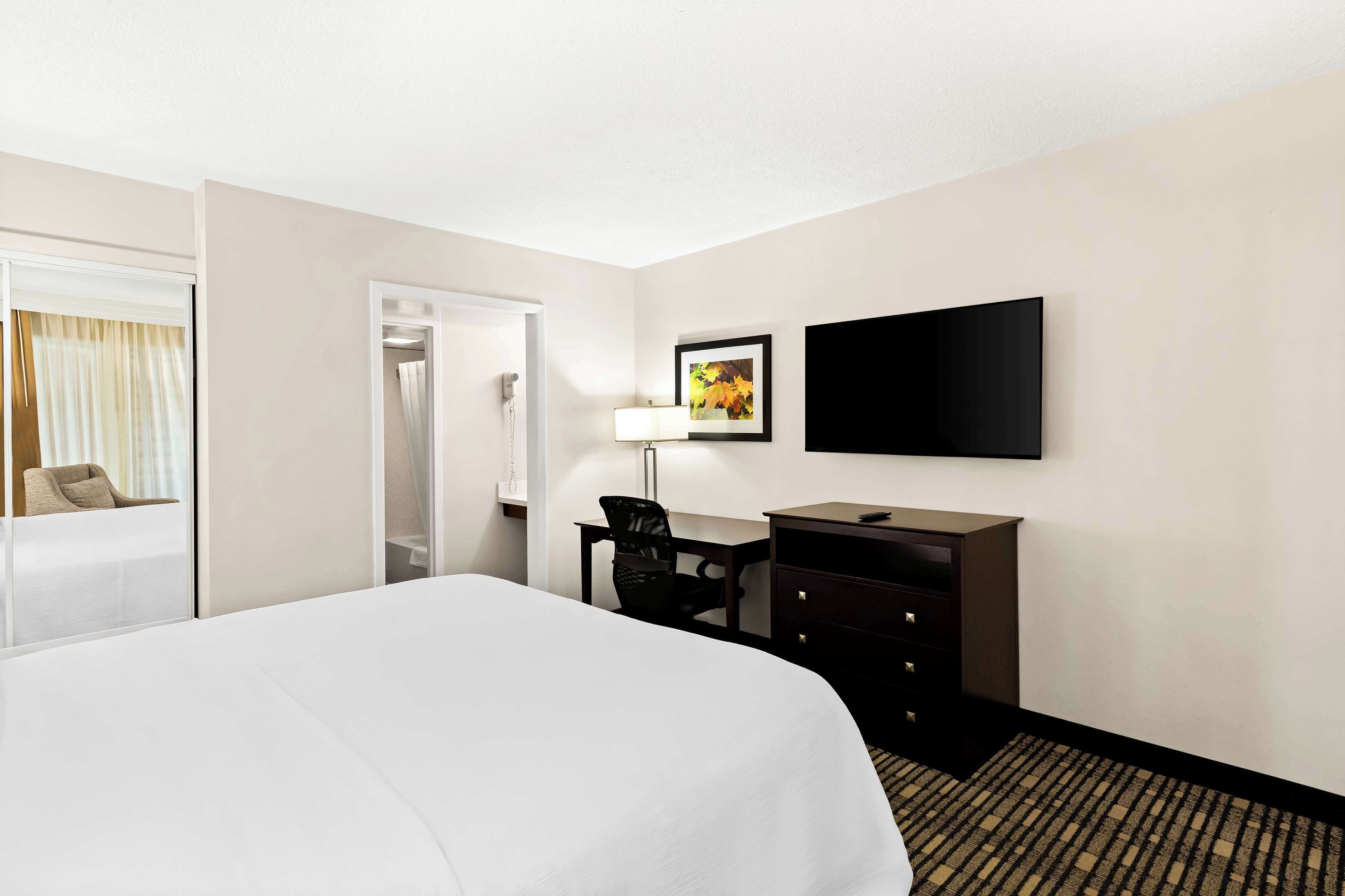 A hotel room with a large bed, a desk with a chair, a flat-screen TV mounted on the wall, and a door leading to a bathroom.