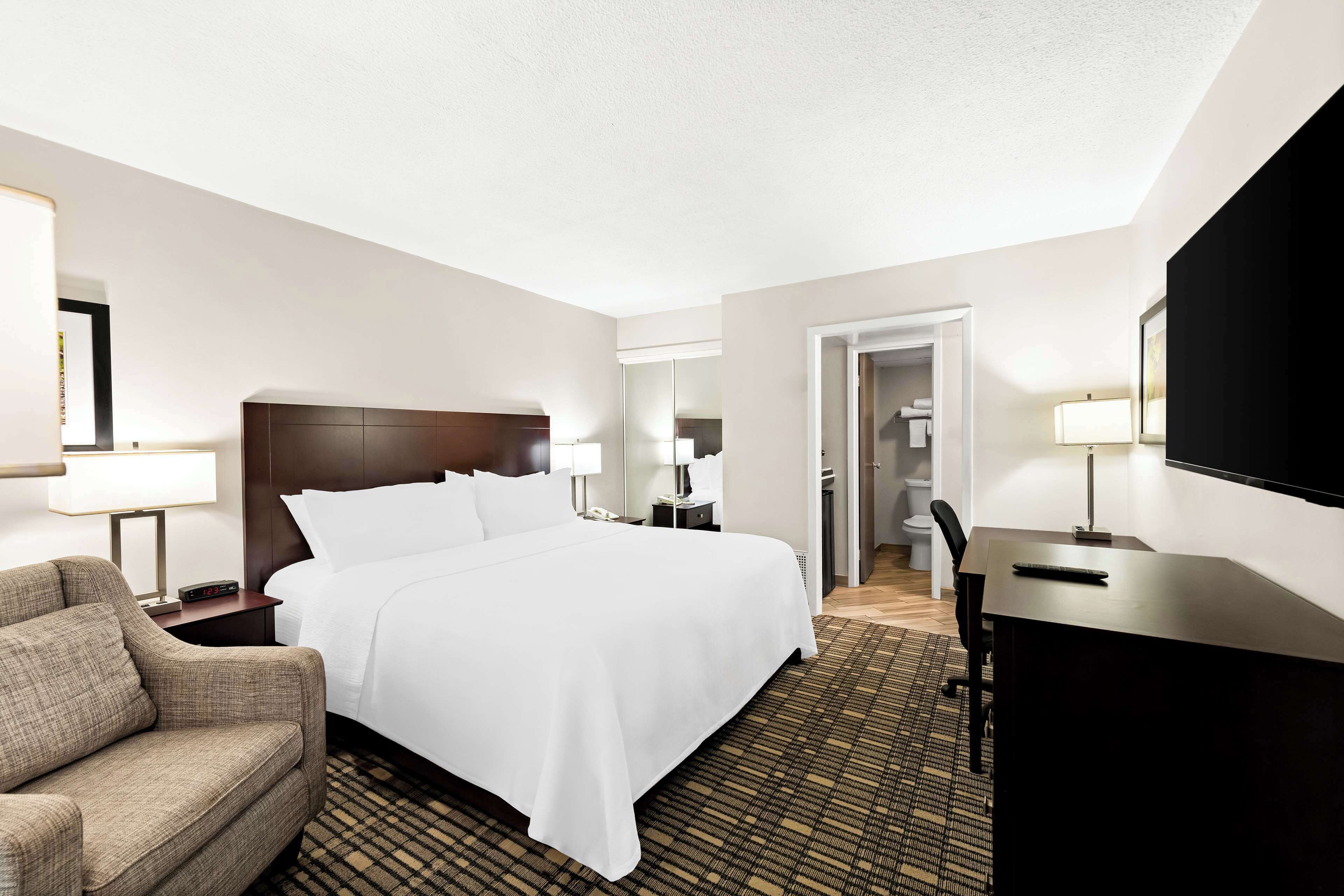 A hotel room with a bed, a desk, a chair, a lamp, and a television.