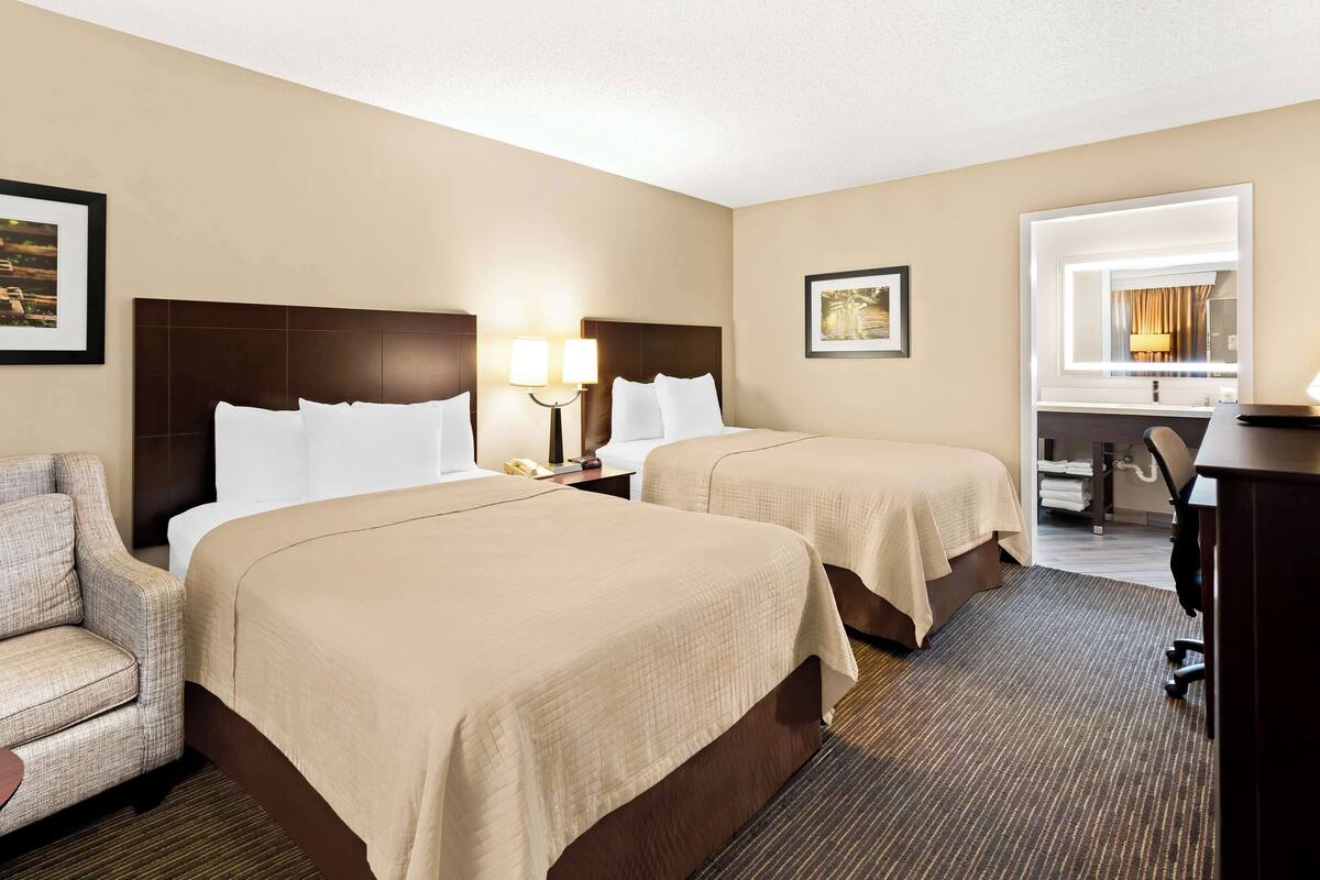 A hotel room with two beds, a desk, a chair, and a large window.