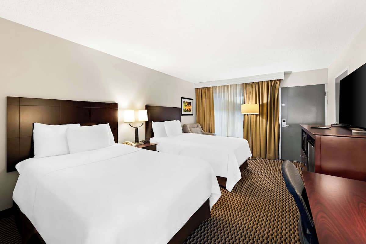 A hotel room with two beds, a desk, a TV, and a window with curtains.