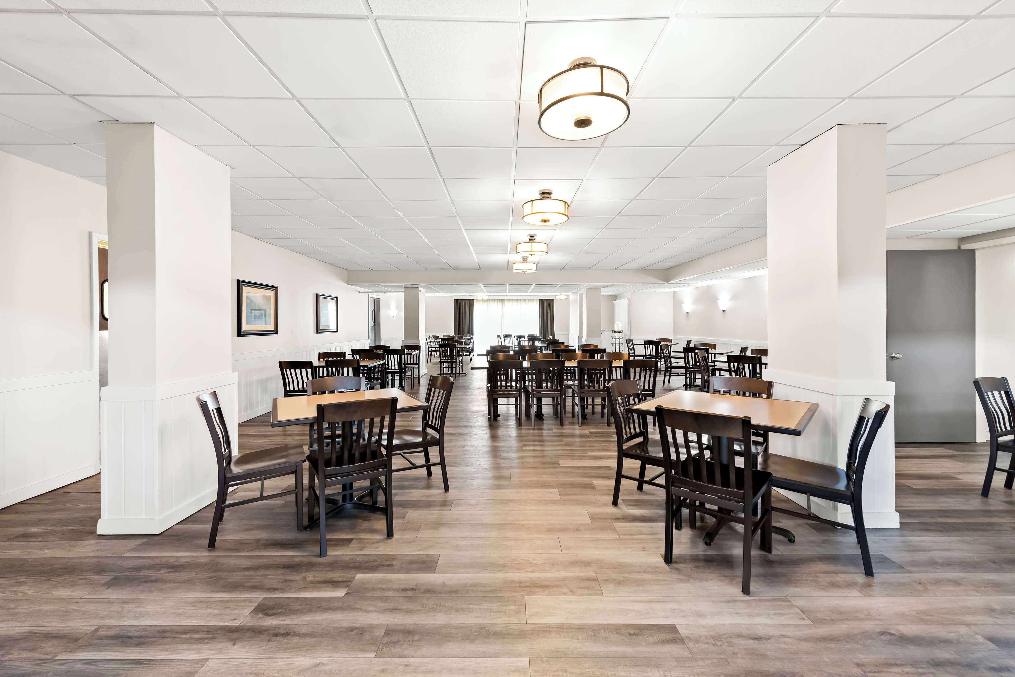 A spacious dining area with multiple tables and chairs, white walls, and a tiled ceiling.