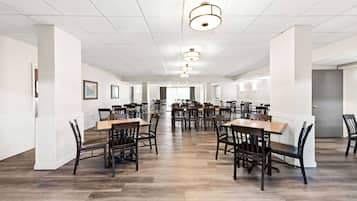 A spacious dining area with multiple tables and chairs, white walls, and a tiled ceiling.