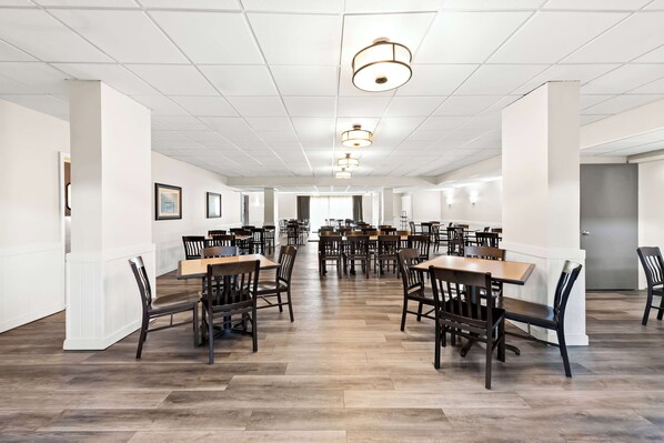 A spacious dining area with multiple tables and chairs, white walls, and a tiled ceiling.