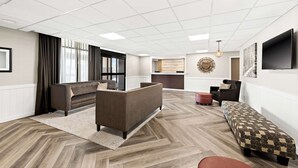 A modern living room with a sofa, ottoman, and bench, a herringbone wood floor, and a large TV on the wall.