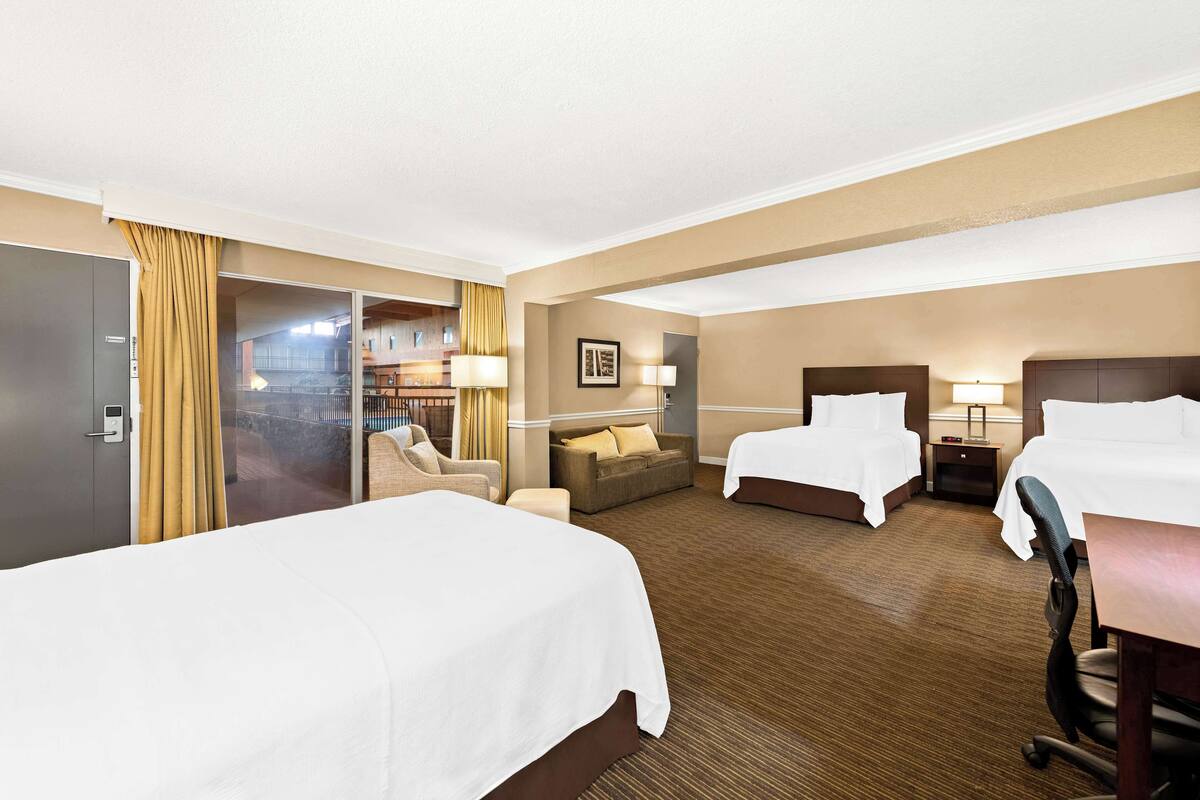A hotel room with two beds, a sofa, a desk, and a chair.