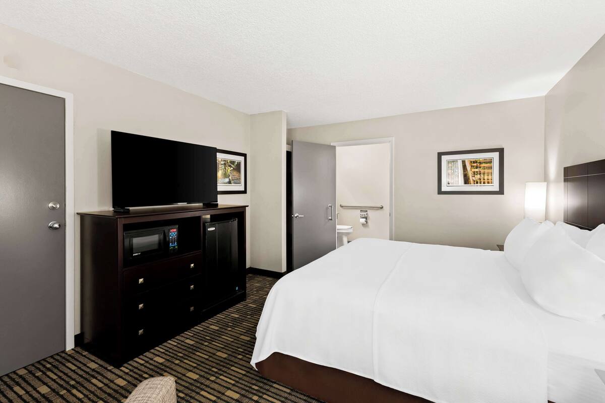 A hotel room with a bed, a TV on a dresser, a bathroom with a sink and mirror, and framed pictures on the wall.