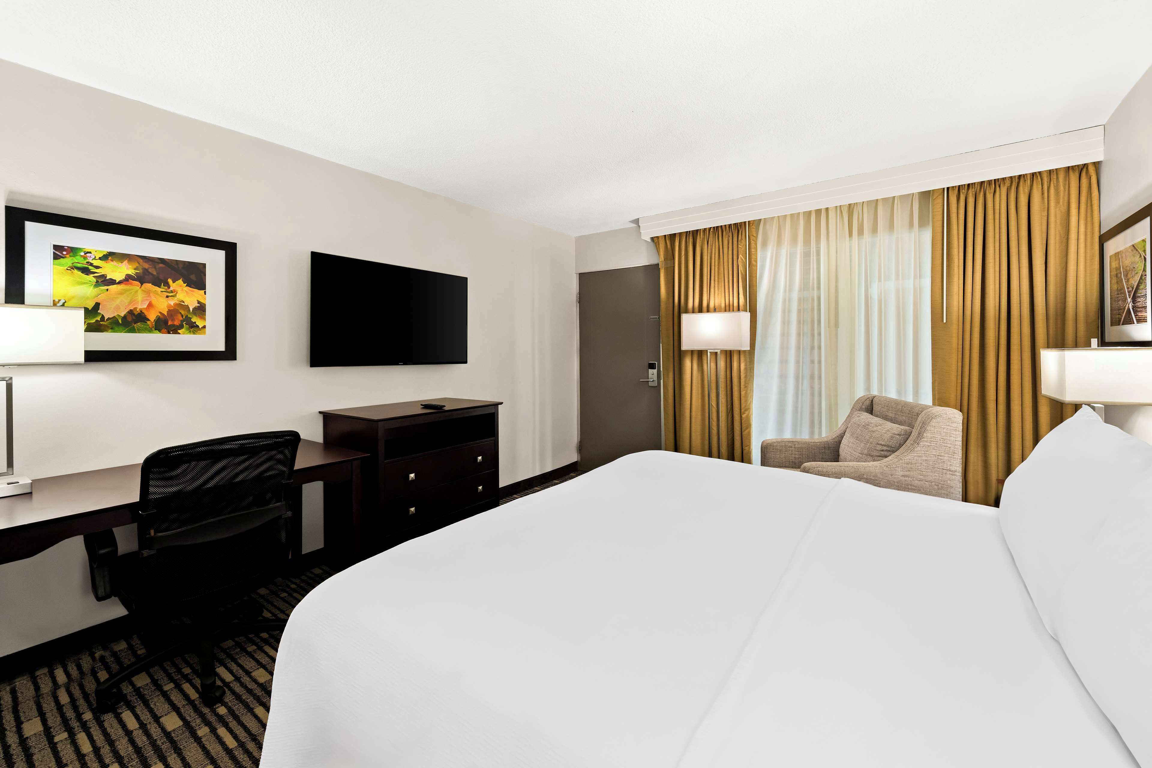 A hotel room with a large bed, a desk with a chair, a television, and a window with curtains.