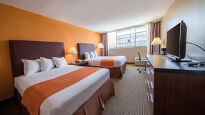 Una habitación de hotel con dos camas, un escritorio con televisor y una ventana con cortinas.