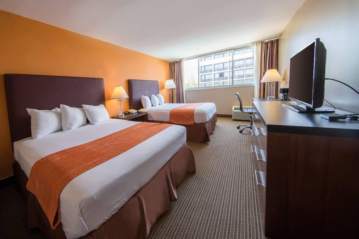 A hotel room with two beds, a desk with a television, and a window with curtains.