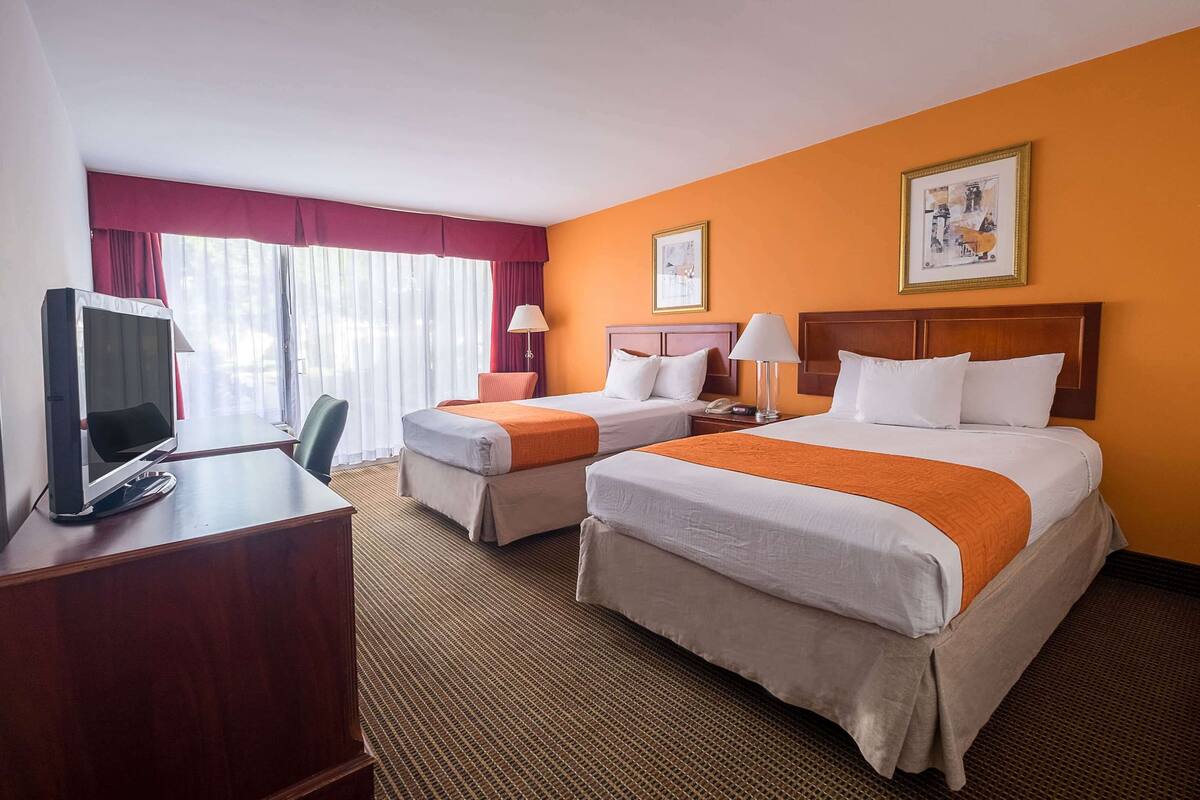 A hotel room with two beds, a desk with a TV, and a window with curtains.