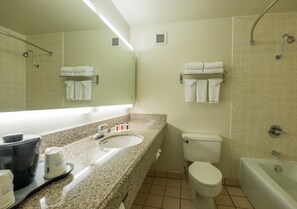 Een badkamer met een wastafel, toilet en bad. Handdoeken liggen op een plank en er is een douche met een greep.