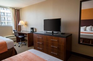 A hotel room with a bed, a desk with a television, a chair, and a lamp.