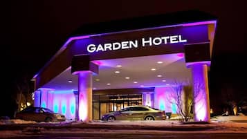 The exterior of the Garden Hotel with illuminated signage and two cars parked in front.