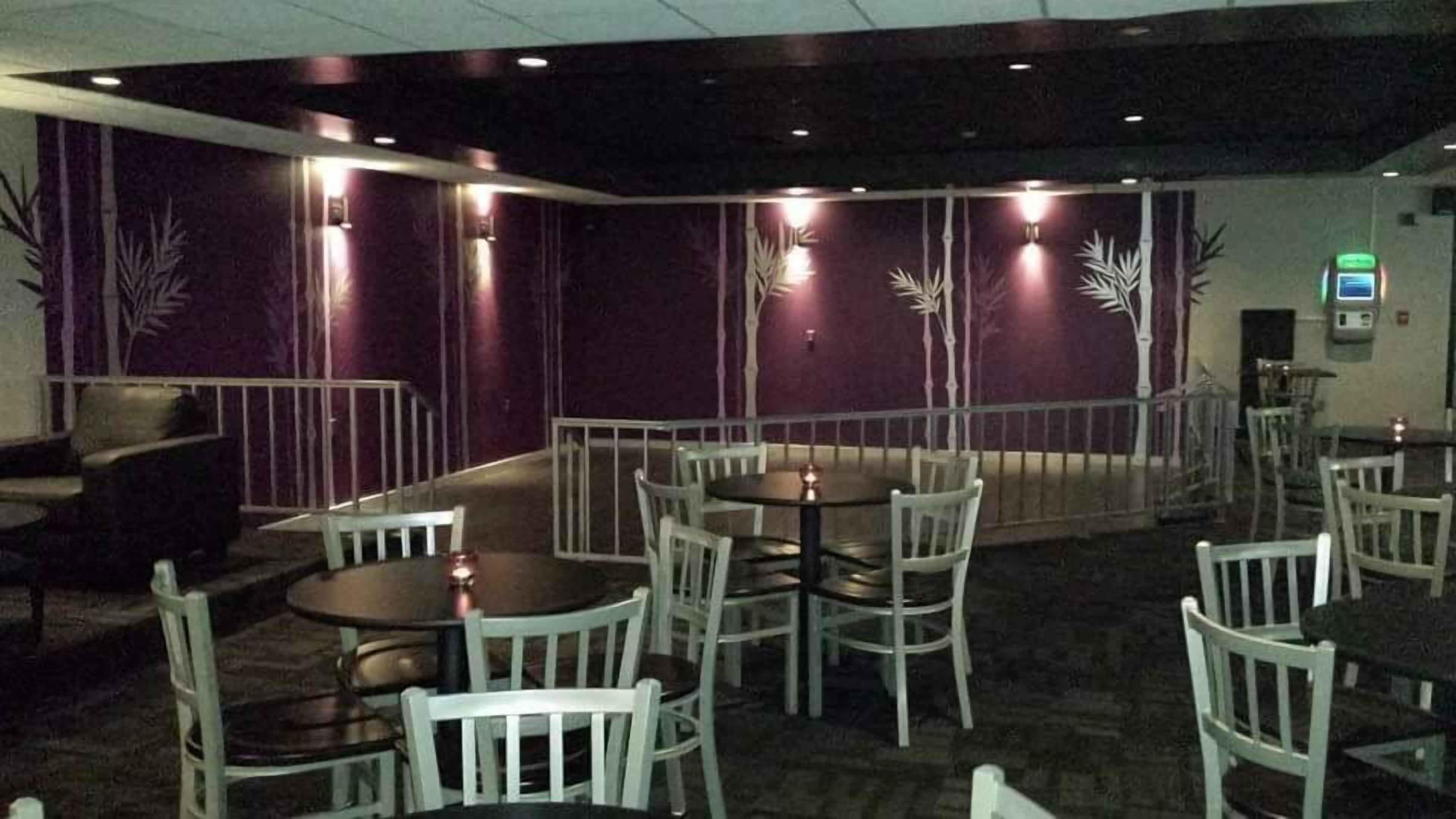 Un restaurant avec des tables rondes et des chaises blanches, des murs violets et des appliques murales décoratives.