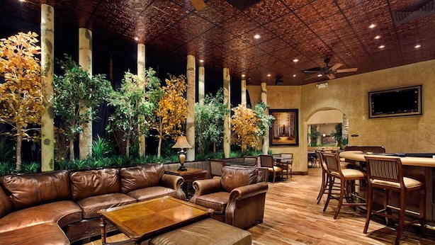 A spacious lounge area with leather sofas, a wooden coffee table, and a bar with wooden chairs. - Maverick Hotel and Casino by Red Lion Hotels (Elko)