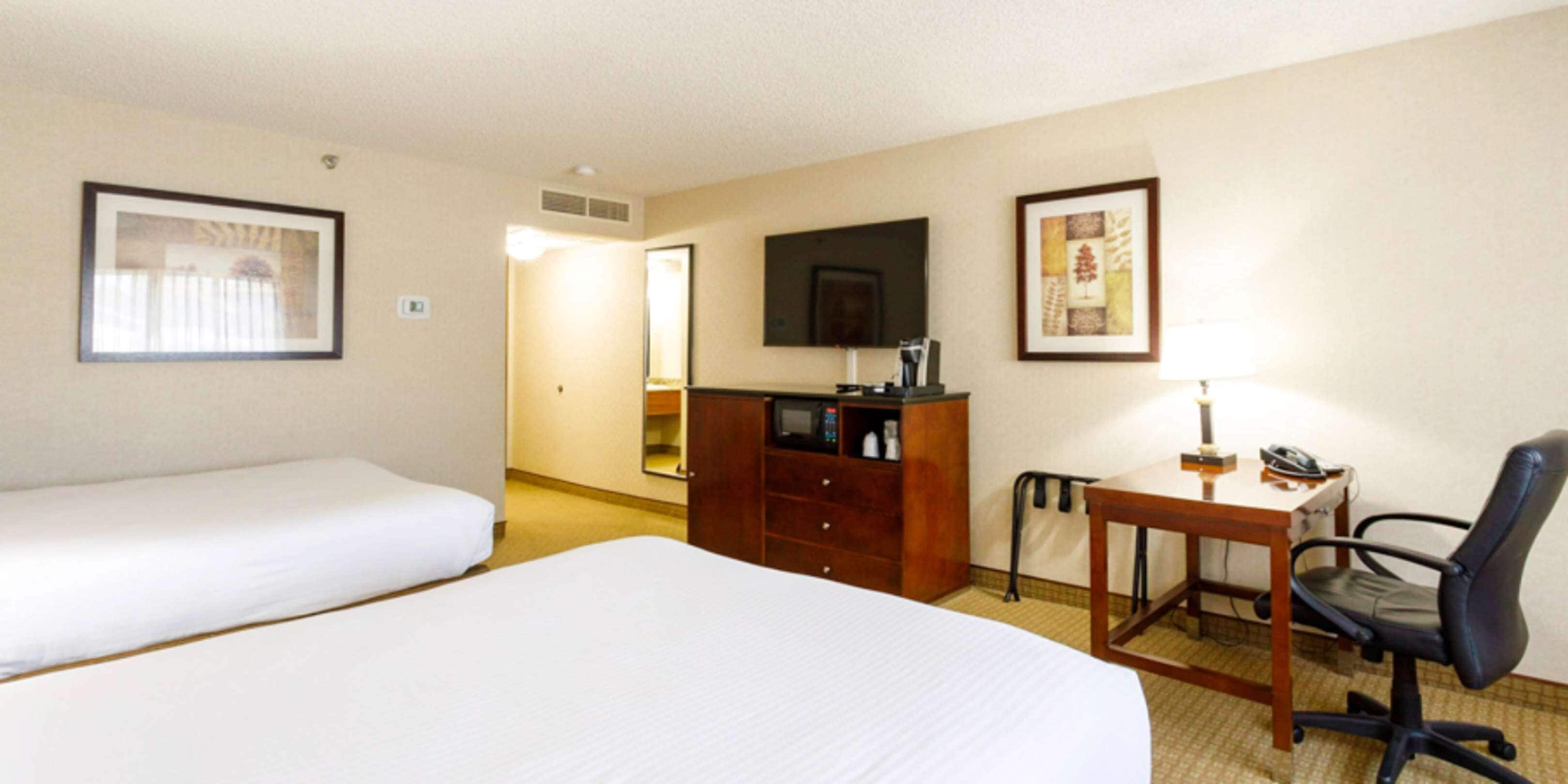A hotel room with two single beds, a wooden desk with a chair, a television, and a minibar.