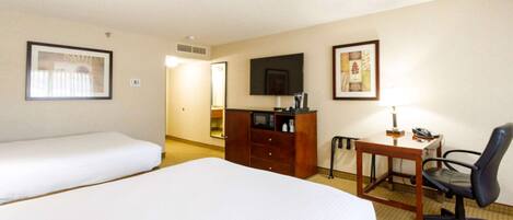 A hotel room with two single beds, a wooden desk with a chair, a television, and a minibar.