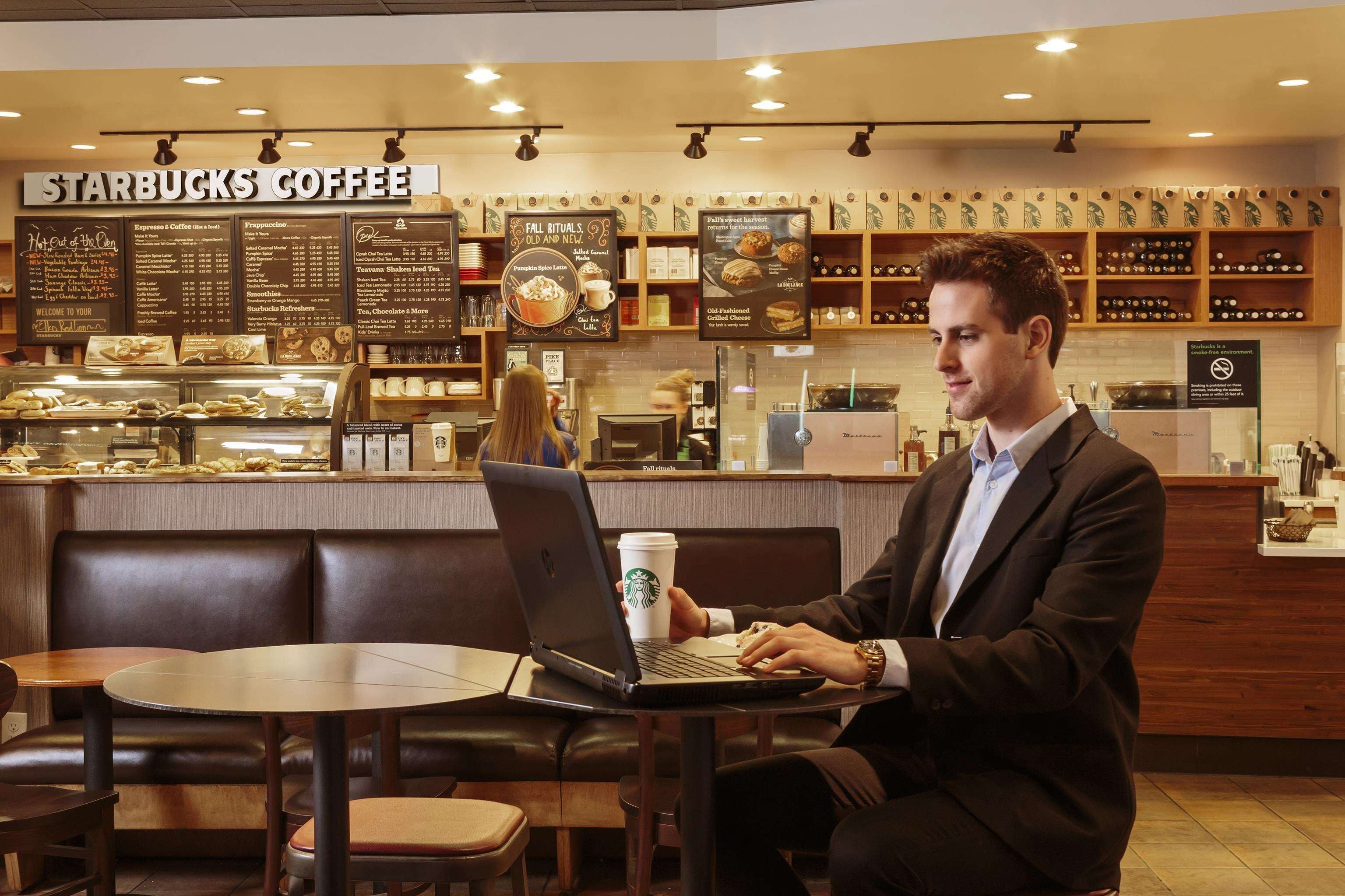 A Starbucks Coffee with a menu board, a laptop on a table, and a person using the laptop.
