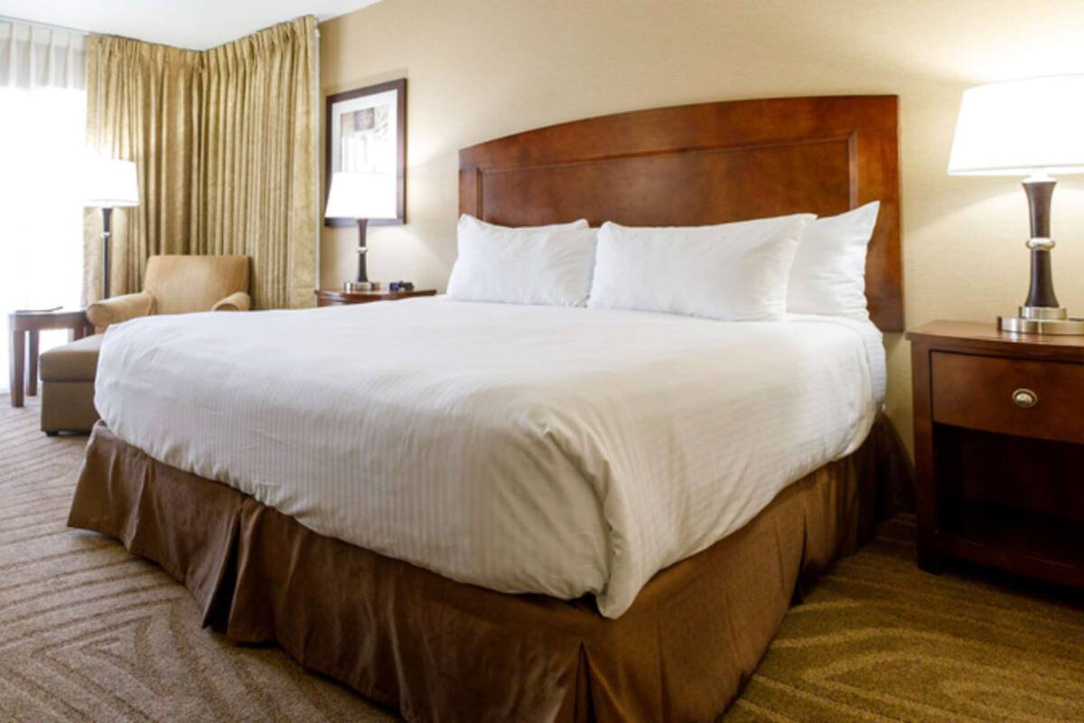 A hotel room with a large bed, a chair, a desk, and a lamp.