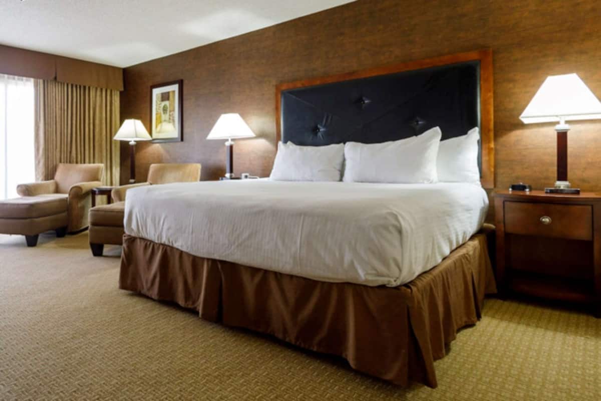 A hotel room with a large bed, two bedside tables with lamps, a chair, a desk, and a large window with curtains.