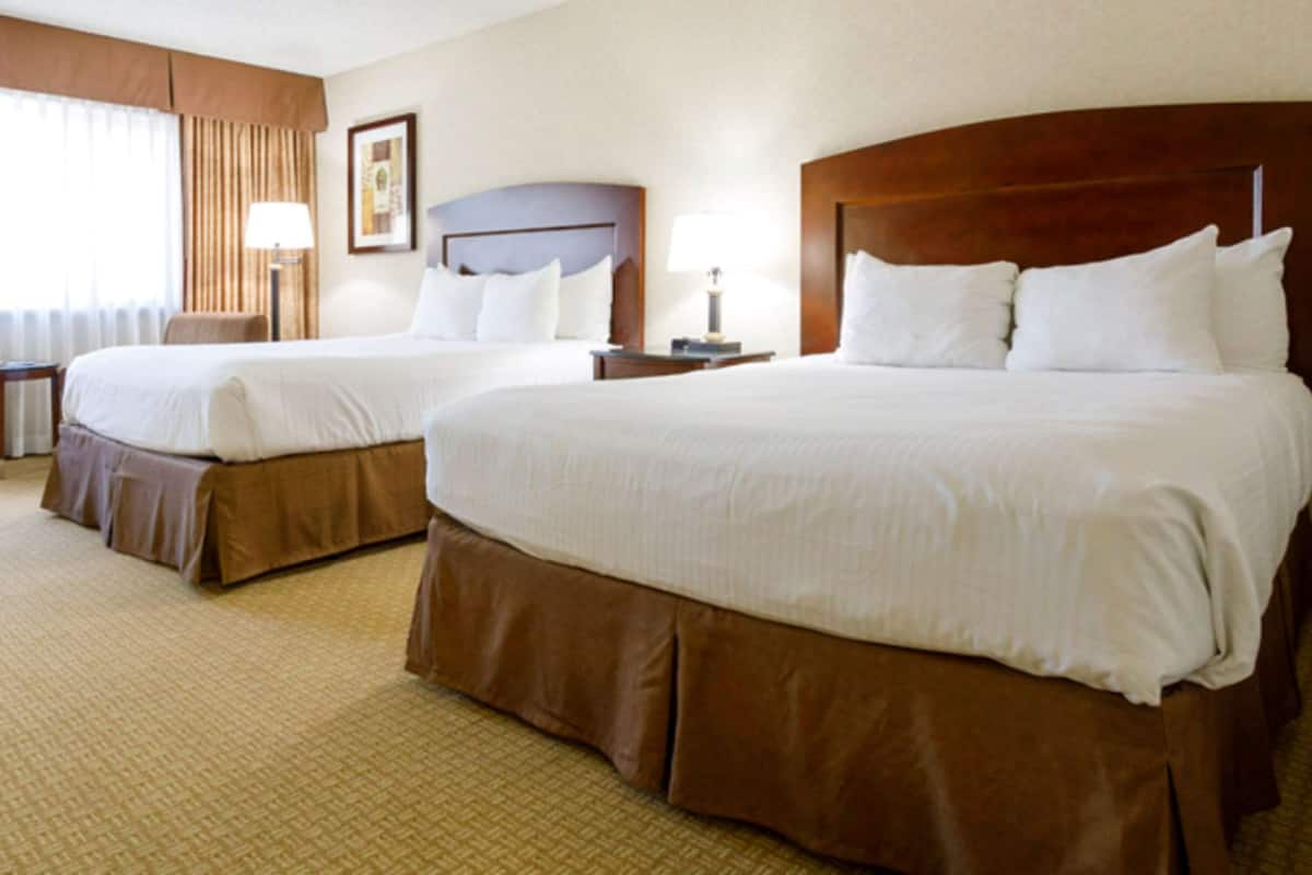 A hotel room with two beds, a small table, a chair, and a lamp.