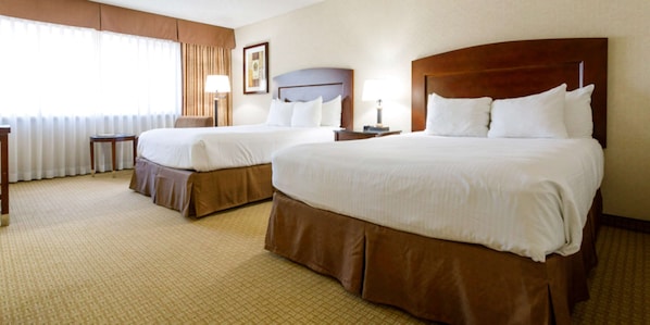 A hotel room with two beds, a small table, a chair, and a lamp.