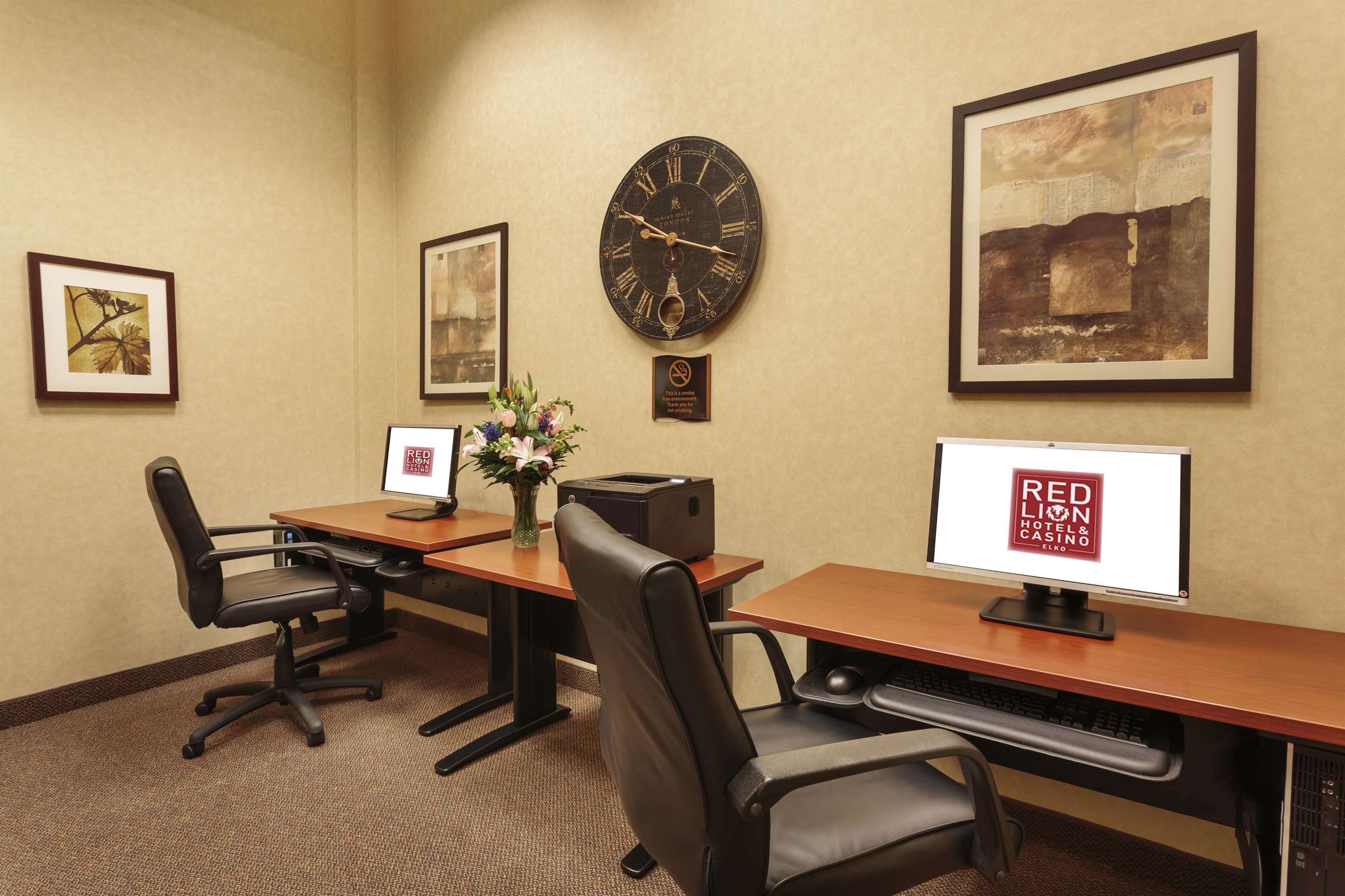 Une salle de conférence équipée de deux bureaux, de chaises, d’une horloge, d’œuvres d’art encadrées et d’une enseigne du Red Lion Hotel & Casino.