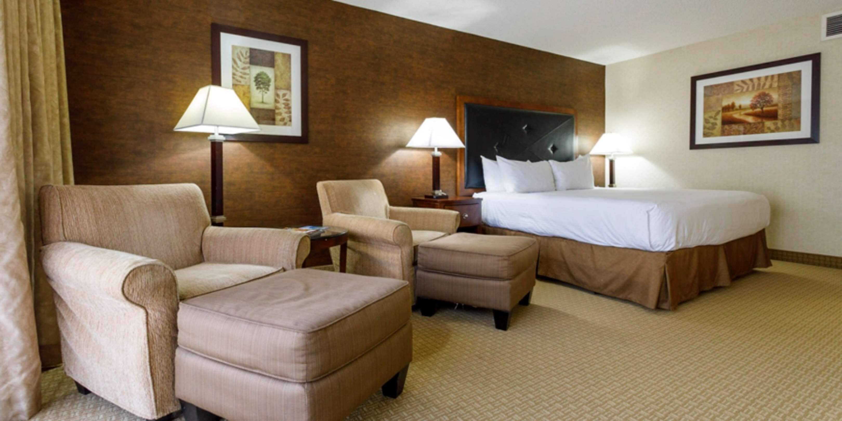 A hotel room with a bed, two armchairs, a small table, and two lamps.