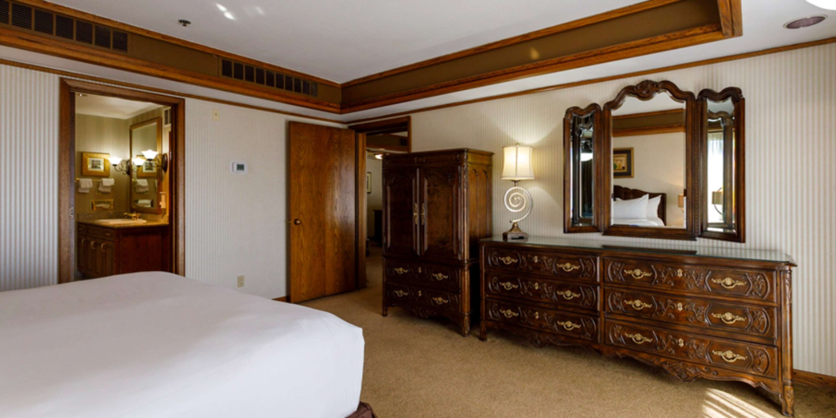 A hotel room with a large bed, wooden dresser, and a mirror.