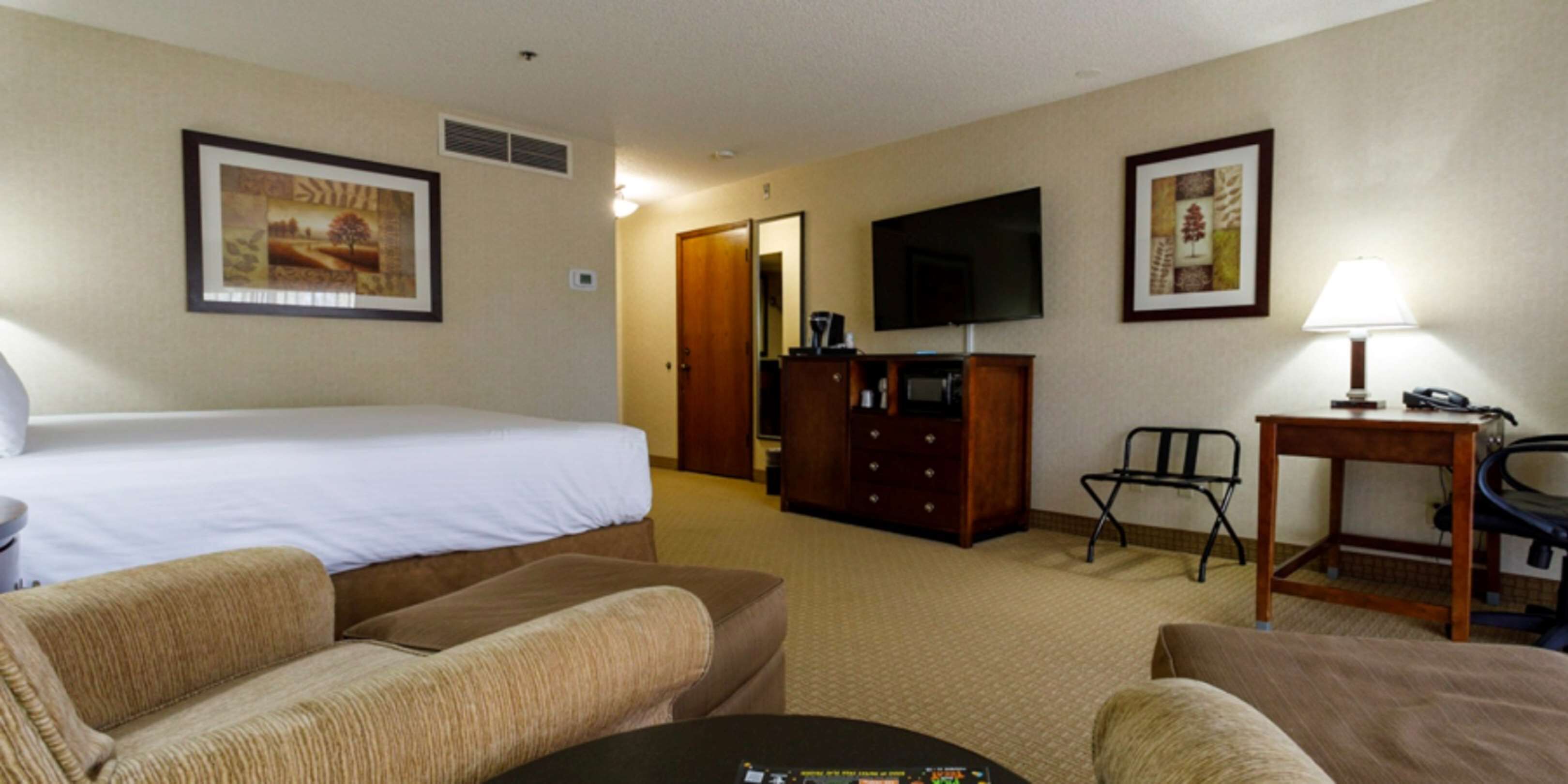 A hotel room with a bed, a sofa, a TV, a desk with a lamp, and a dresser.