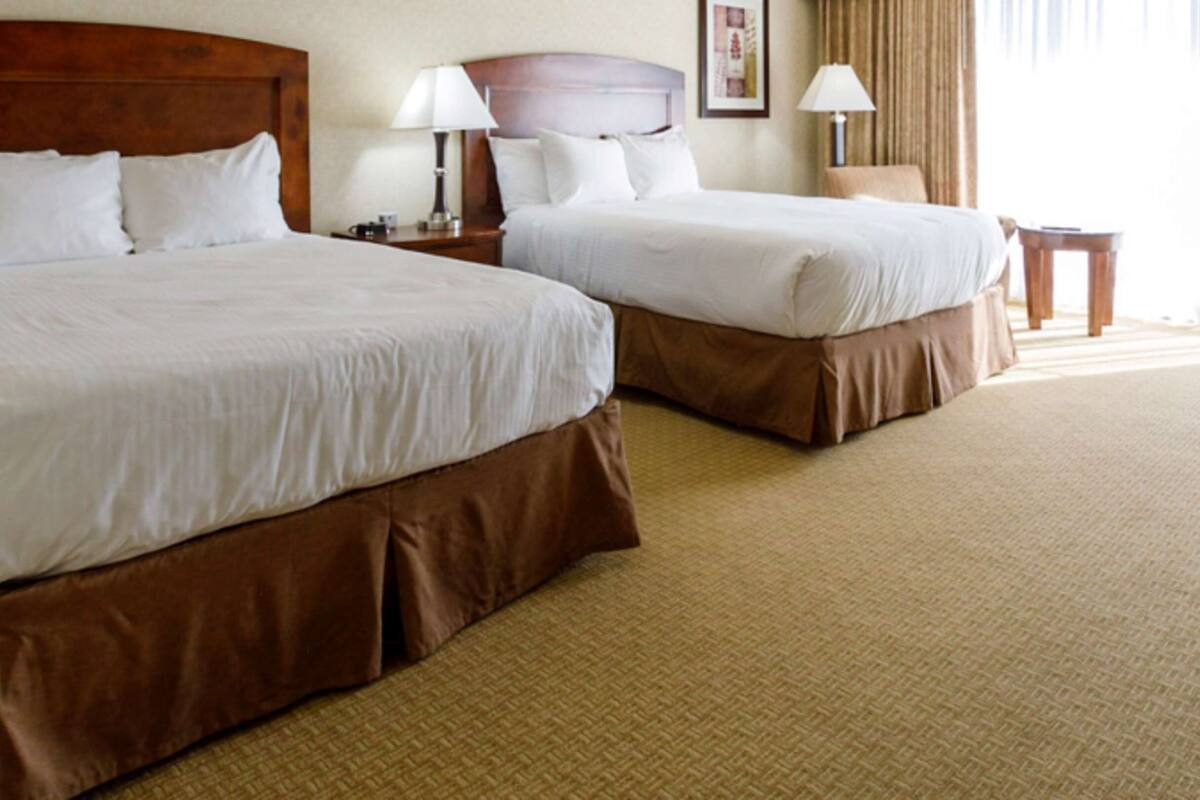 Two double beds with brown headboards and white bedding in a hotel room.