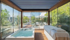 A spa area with a hot tub, a massage table, and a view of the city through large glass windows. - Le Bristol Paris - Oetker Hotels (Paris)